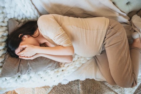 View from above of sleeping pregnant woman covering eyes with hands and relaxing on couch at home,