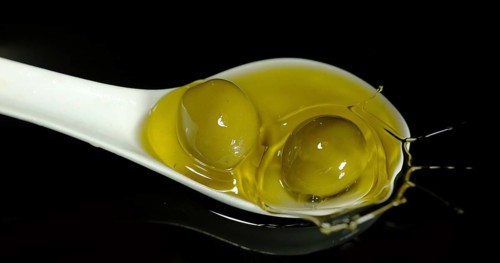 Green Olive, Olea europaea, Falling in a Spoon against Black Background