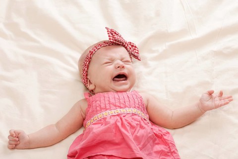 Crying and gesturing ten weeks old baby girl on bed