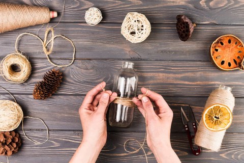 Female hand tying glass bottle with string near cutter dry lotus pod dried fruit slices pine cone