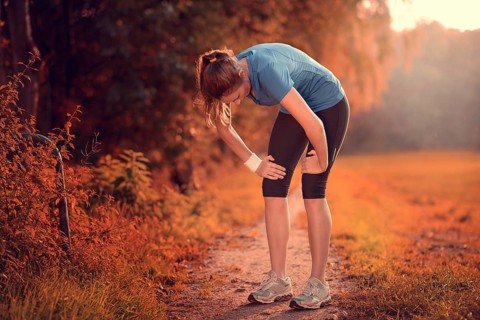Young athletic woman taking a break from training standing resting her hands on her knees on a