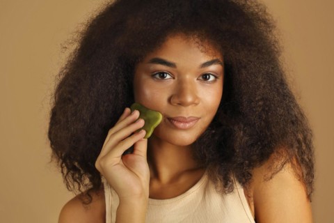 Gorgeous dark skinned model gently weeps Gua sha stone up cheekbone massaging her face to help