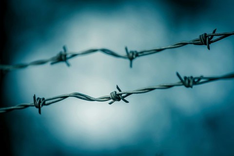 Barbed wire on a metal fence to demarcate the border, closeup, blurry background