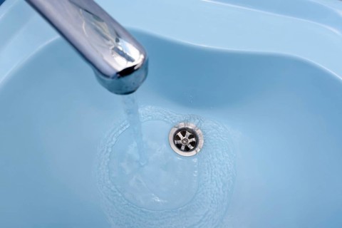 Water flows from the tap in a blue washbasin. The liquid pours out, swirling, in the open plug