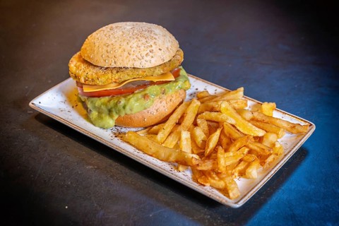 Vegan burger with guacamole and fries on a white plate on a black background