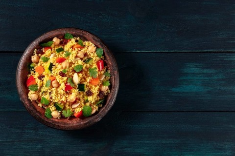 Vegan couscous with vegetables, almonds, chickpeas and herbs, shot from above on a dark wooden