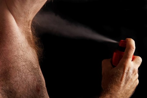 Man with chest hair spraying deodorant into his armpit