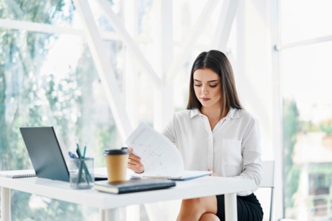 Pretty businesswoman sitting at workplace and reading documents in her modern office. Woman in