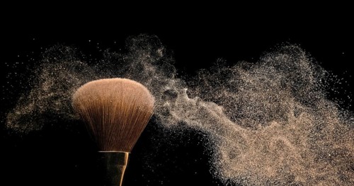 Make-up Brush spreading blush powder on black background