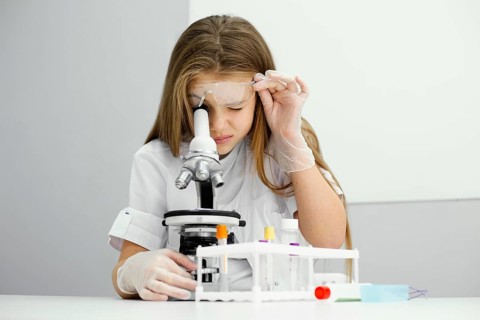 Front view curious young girl scientist using microscope