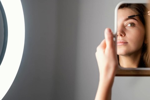 Woman brushing her eyebrows while looking mirror after treatment with copy space