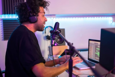 Side view of a musician recording a podcast using microphone and laptop
