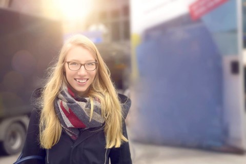 Smiling attractive blond woman wearing glasses dressed in warm winter fashion standing in an urban