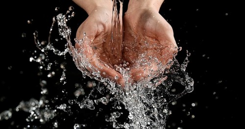 Hands of Woman and Water against Black Background