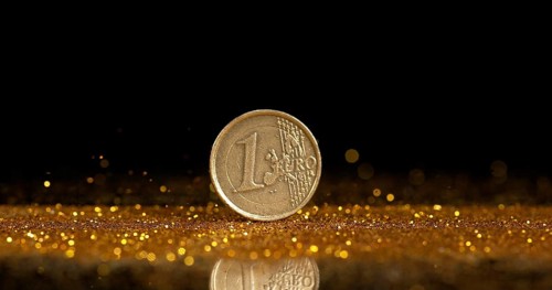 Coin of 1 Euro Rolling on Gold Powder against Black Background