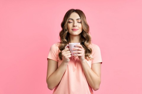 Young pretty woman enjoying cup of aroma coffee closed eyes on pink background. Relax and rest