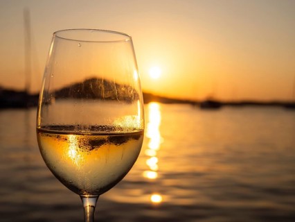 Sunset shimmering through a glass of white wine, evening mood in the harbour, boats and sailing