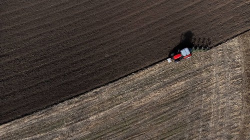 A red tractor ploughs a harvested field, dark soil, bird's eye view, drone shot, Upper Bavaria,