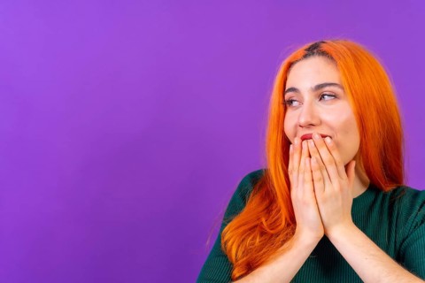 Redhead woman in studio photography making the gesture please on a purple background