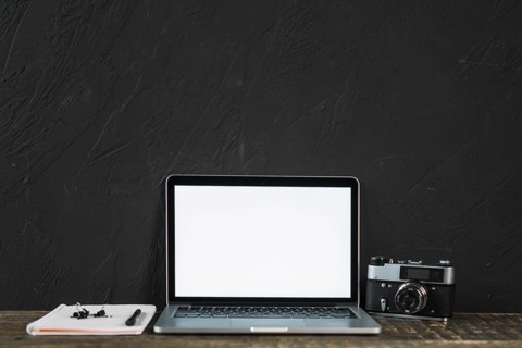 Retro old camera blank screen laptop with stationeries wooden table