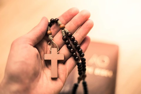 Man is holding a rosary, bible in the background