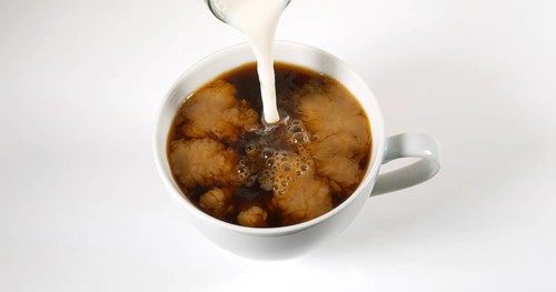 Milk poured into a Cup of Coffee against White Background