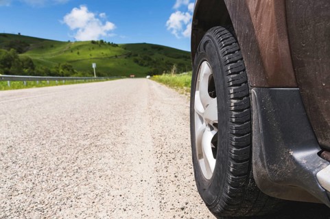 Close-up of a SUV wheel on an asphalt road outside the city against the green hills of blue sky and