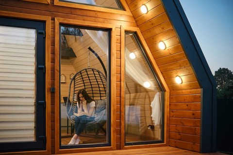 Woman relaxing in a hanging chair with a book inside a stylish wooden cabin. The warm lighting and