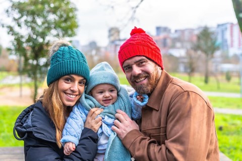 Smiling parents holding their baby, wearing winter clothes and wool hats, having fun together in a