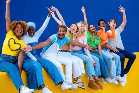 Happy multi-ethnic friends raising hands and smiling sitting in an outdoor wall