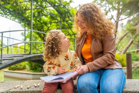 Cute blonde girl reading a book with her mother in the park