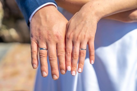 A couple is holding hands and wearing wedding rings. The man's ring is on the left hand and the