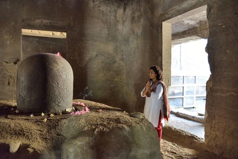 Woman praying in front of the Shiva Lingam, a phallic symbol, in the main cave of the Shiva temple,