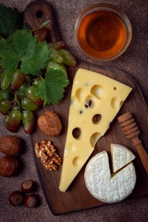 Cheese with big holes, emmental, maasdam, brie cheese, on a cutting board, with grapes and honey,