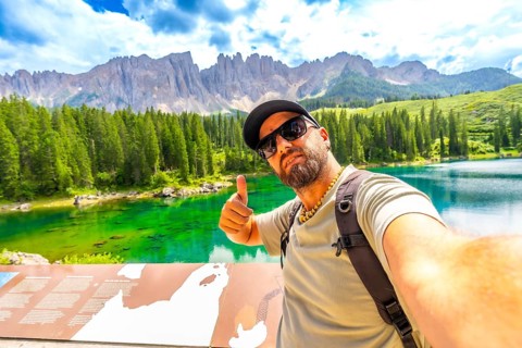 Tourist enjoying the breathtaking view of lake carezza and the dolomites making selfie and thumbs