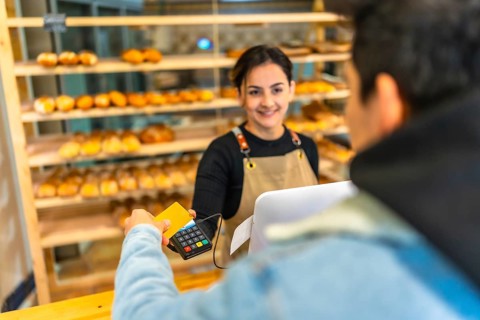 View over shoulder of a young man paying using credit card in a bakery shop