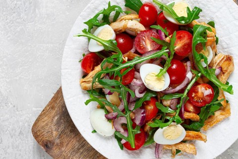 A warm salad with fried chicken fillet, arugula and cherry tomatoes, and boiled quail eggs, on a