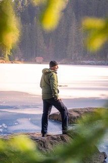 Person standing on the shore of a frozen lake, framed by rocky shore and forest, Glaswaldsee, Bad