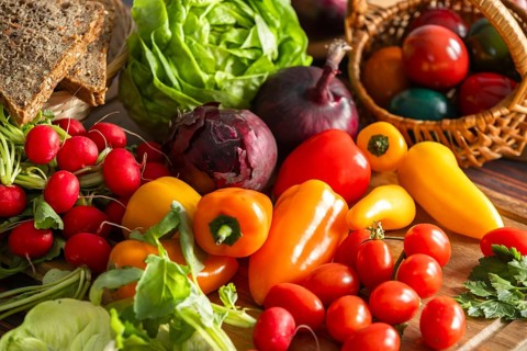 Colourful fresh vegetables, including peppers, tomatoes and radishes, surrounded by bread and