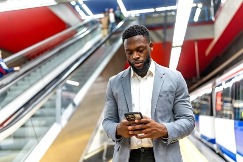 Young businessman waiting for a subway train in a station, using his smartphone to check messages