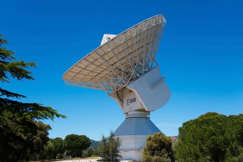 ESA's large radio telescope under a clear blue sky, surrounded by green trees, for scientific use,