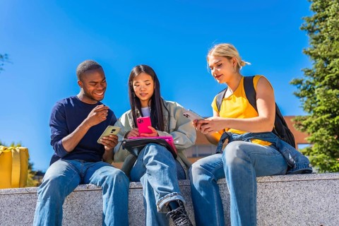 Low angle view photo of a multiracial group of students using smartphones sitting outside the