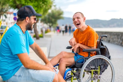 A disabled person in a wheelchair with a friend on summer vacation having fun laughing a lot by the