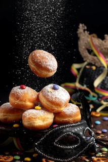 Doughnuts are sprinkled with icing sugar, surrounded by a mask and colourful decorations, carnival