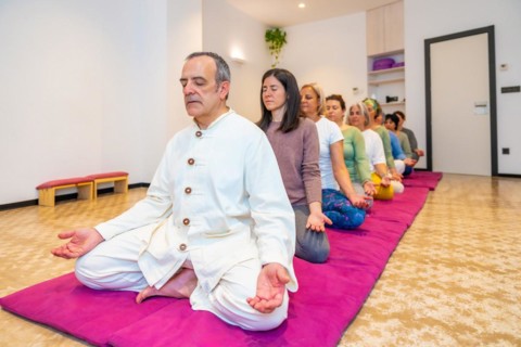 Yoga teacher leading a group of women meditating in line in lotus position and eyes closed