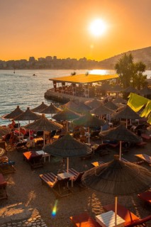 Beautiful resort with umbrellas and palm trees by the sea at sunset in Sarande or Saranda on the