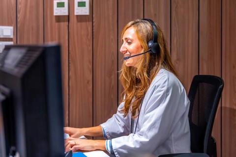 Hospital nurse receptionist talking to patient at registration counter using headset and computer