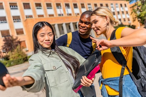 Multi-ethnic university students gesturing success with fingers while taking selfie at the campus
