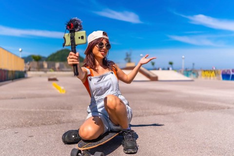 Chinese female young vlogger recording online video with mobile phone while skating in an urban