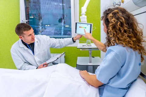 Doctor explaining results to a patient on hospital bed using hanging tablet on the room